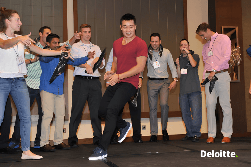 Danny Lim breakdancing on stage at a Deloitte University training in Westlake, Texas, as a circle of colleagues cheers him on